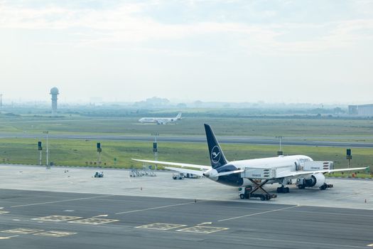 Wide view of commercial airplanes stationed on the airport tarmac with a misty runway backdrop.