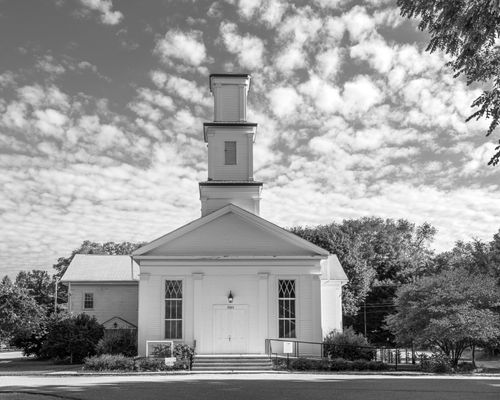 Free Classic white church building with steeple in Michigan, surrounded by trees, beneath a cloudy sky. Stock Photo