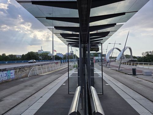 Free A sleek tram station leading to an elegant modern bridge under a cloudy sky. Stock Photo