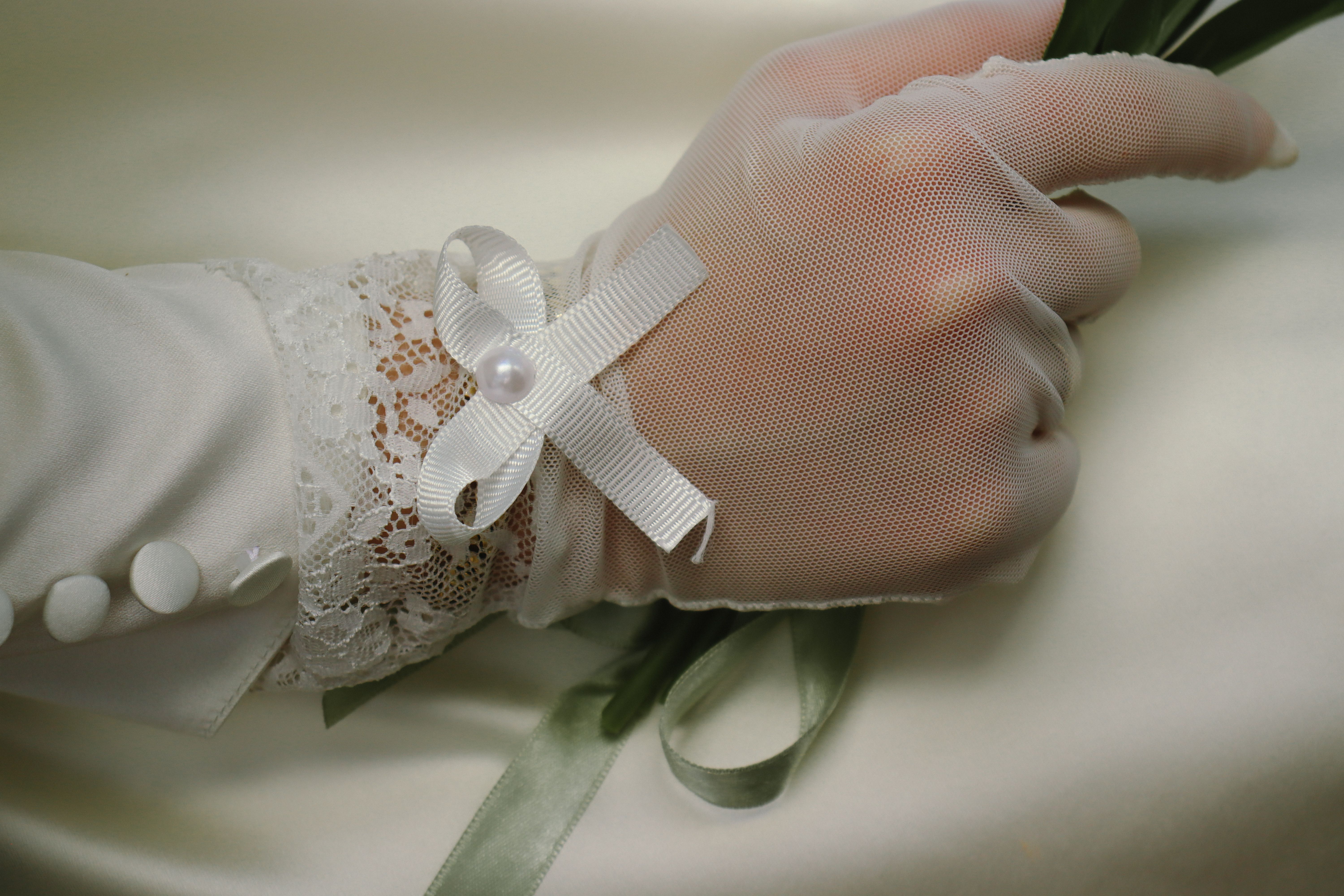 Close-up of a bride's hand in lace glove holding ribbons, showcasing elegance and detail.