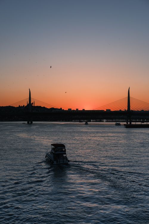 Free A tranquil sunset over a bridge with a boat silhouette, capturing peaceful waters and vivid colors. Stock Photo