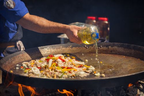 Free Chef pouring oil over a sizzling seafood and vegetable medley on an open flame outdoors. Stock Photo