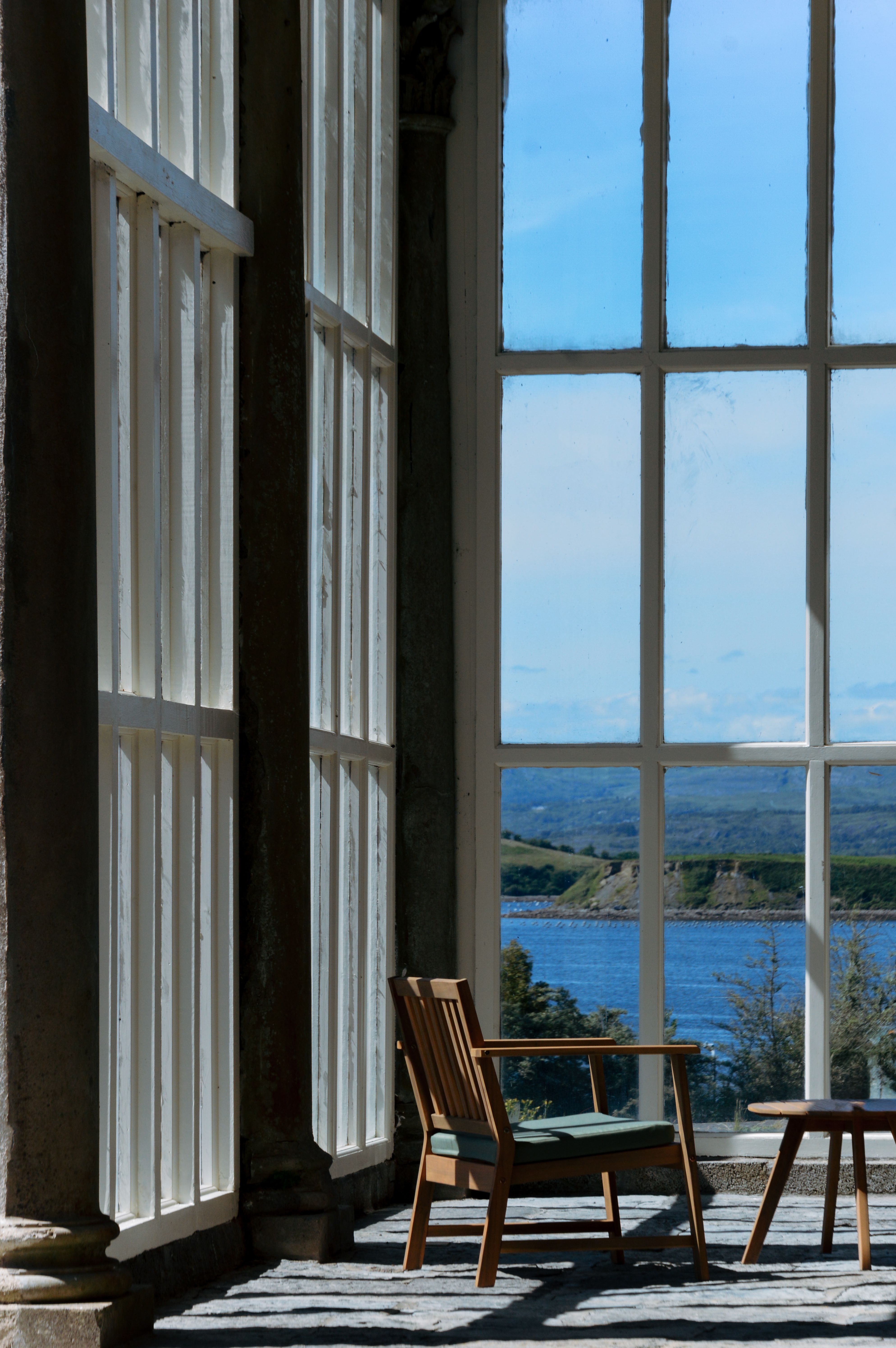 A tranquil view of the coast from a sunlit modern interior with wooden furniture.