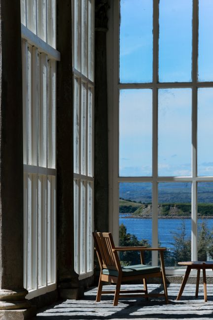 A tranquil view of the coast from a sunlit modern interior with wooden furniture.