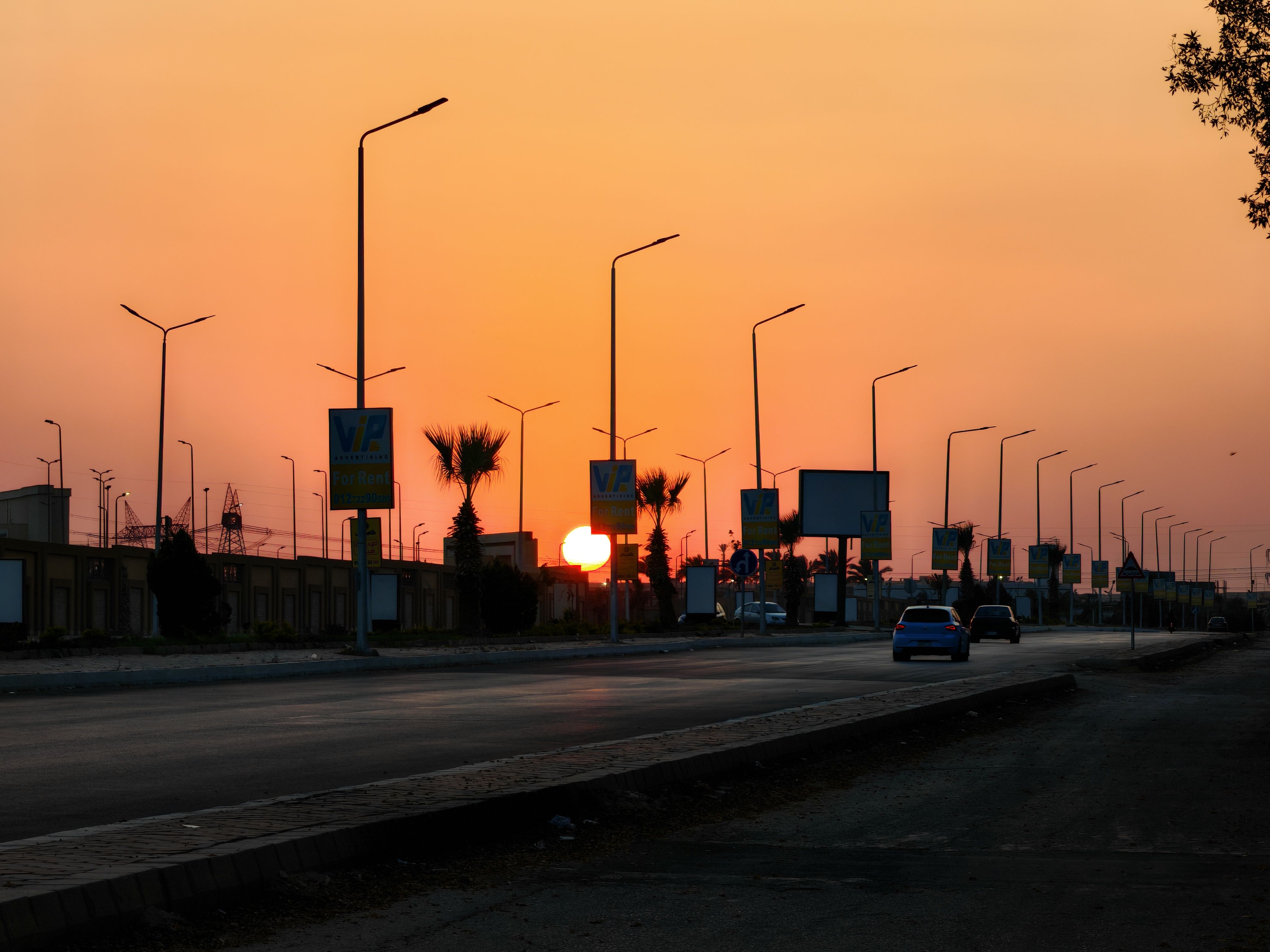 A scenic view of a city street at sunset with silhouetted street lights and palm trees.
