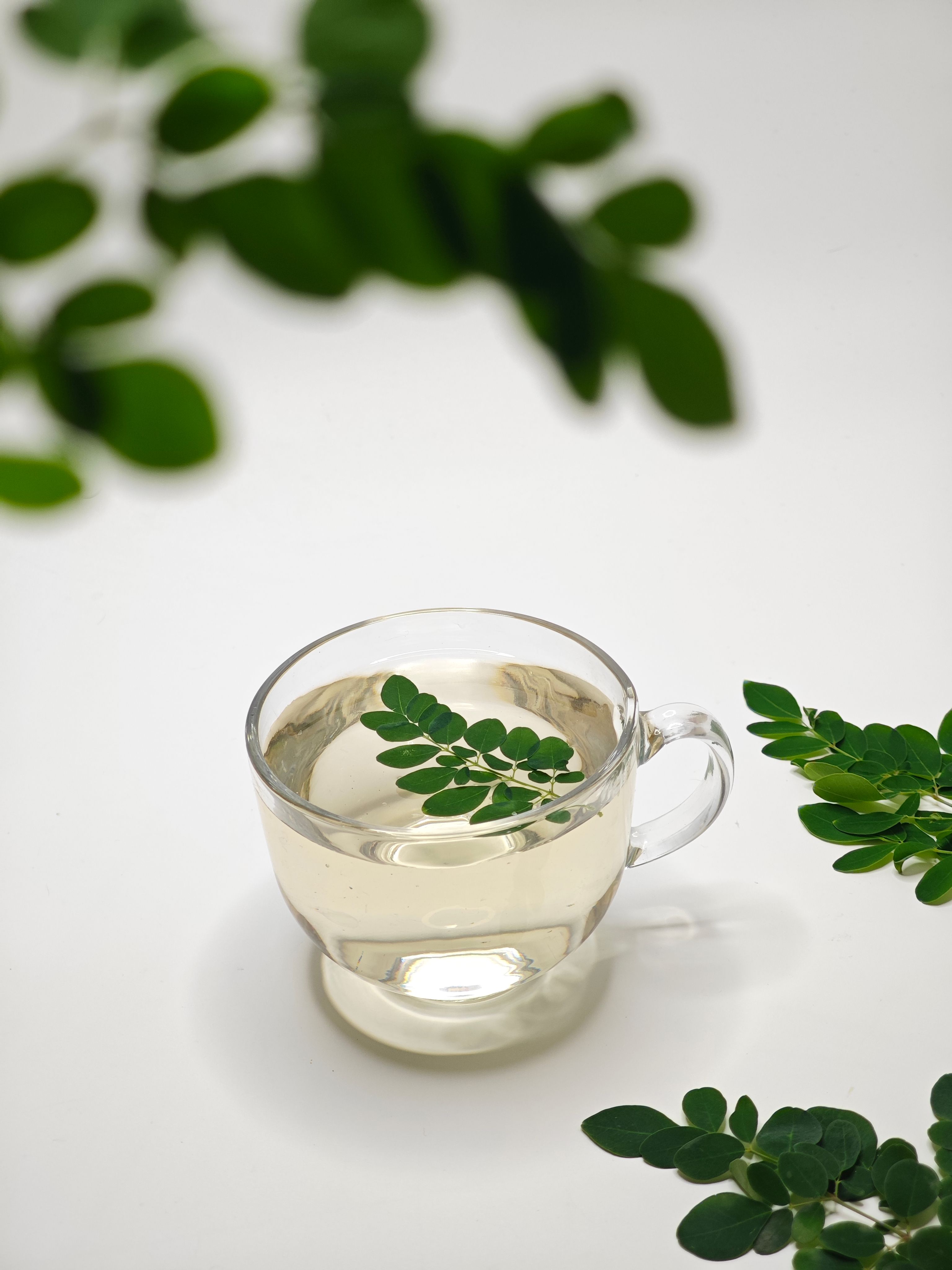 Fresh moringa leaves displayed beside a glass of moringa drink