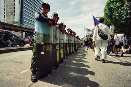 Free Police officers forming a line during a city protest, with demonstrators approaching. Stock Photo