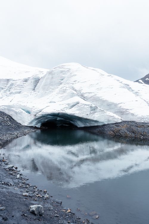 Free A breathtaking view of a glacier cave reflected in a tranquil pool under an overcast sky. Stock Photo