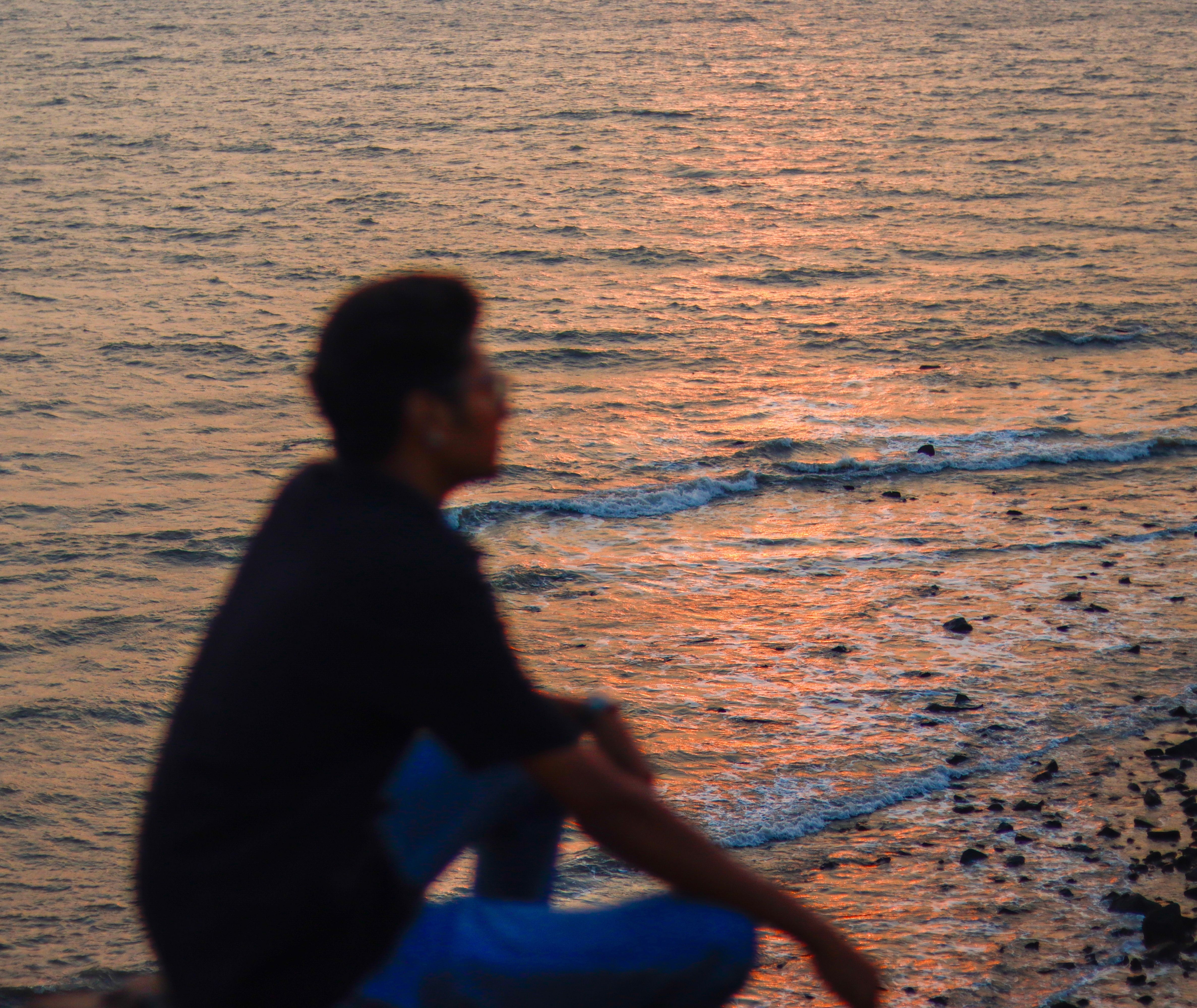 Person sitting by ocean at sunset, reflecting on the horizon.