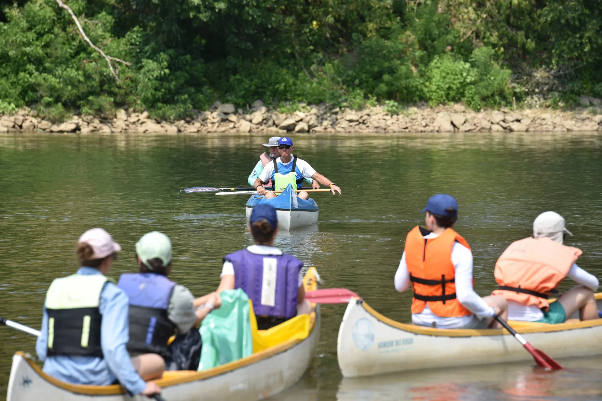 A group canoeing on a scenic river with green banks. A group canoeing on a scenic river with green banks.