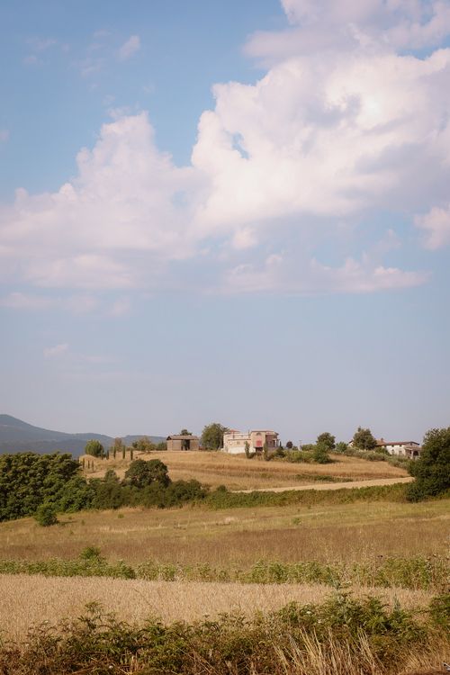 Free Peaceful rural landscape in Italy with rolling fields and distant hills beneath a blue sky. Stock Photo