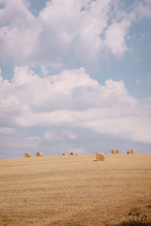 Free Picturesque view of hay bales on a Tuscan field under a bright, partly cloudy sky. Stock Photo