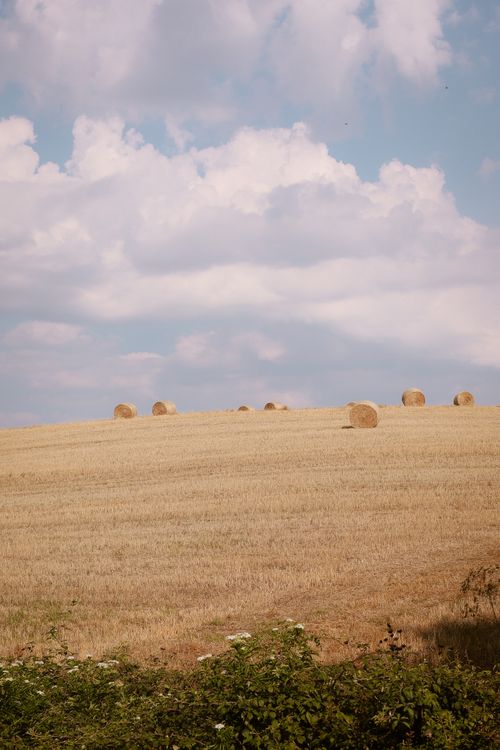 Free Serene Italian countryside with hay bales under a cloudy sky, perfect for travel and nature themes. Stock Photo