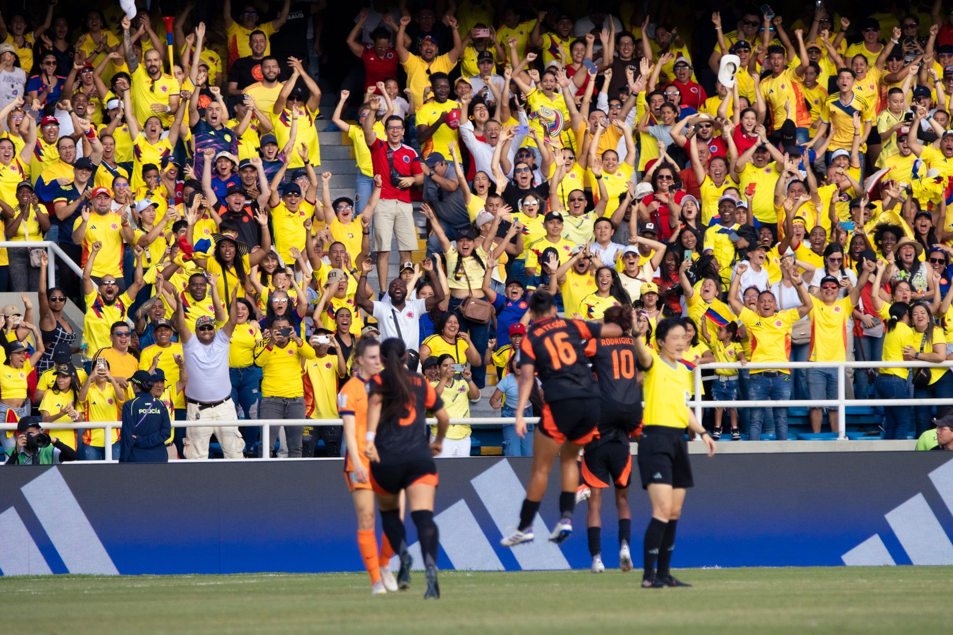 Energetic crowd of Colombian football fans cheering at a match in a vibrant stadium.