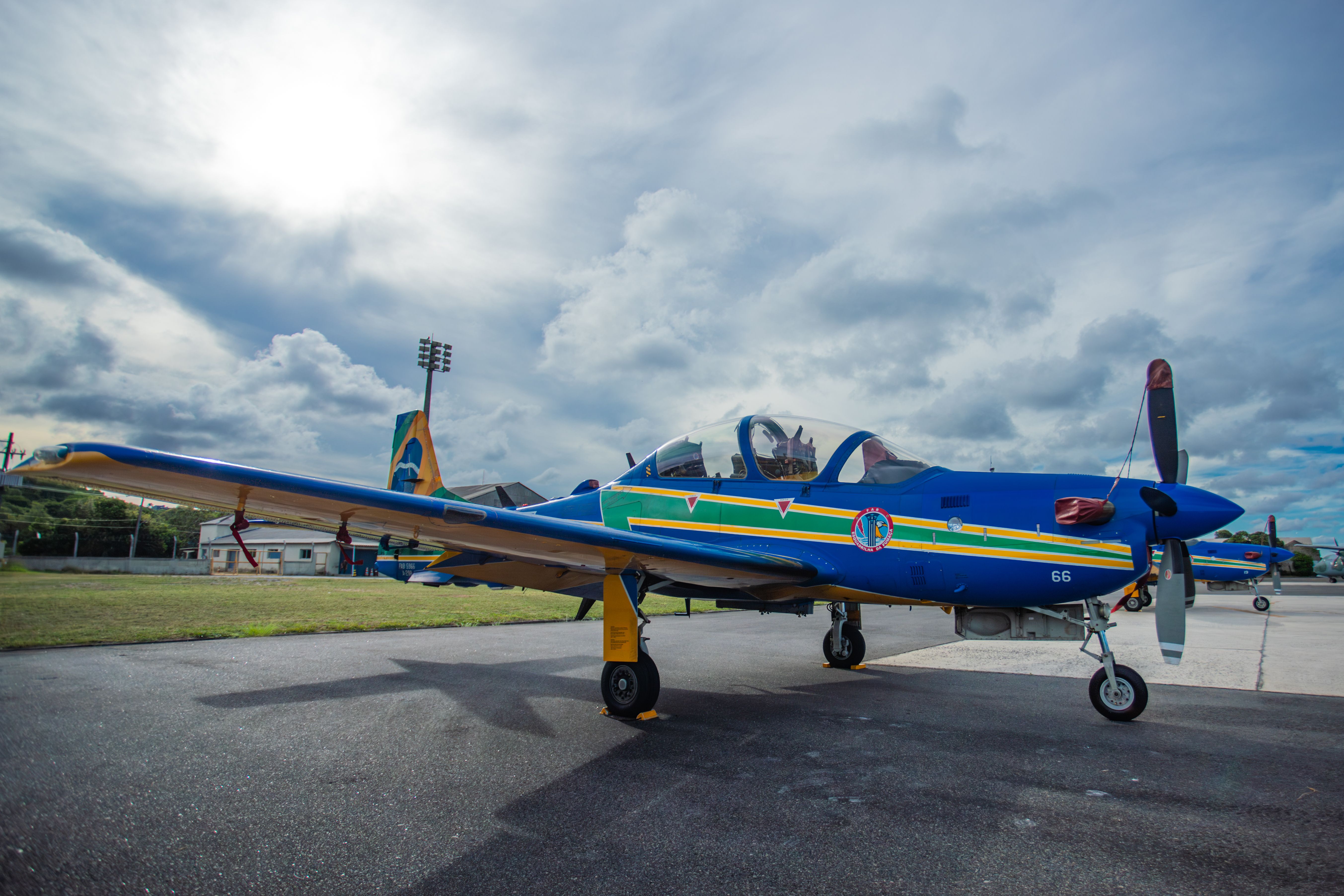 Vibrant blue and yellow training aircraft parked on an airfield under a cloudy sky.