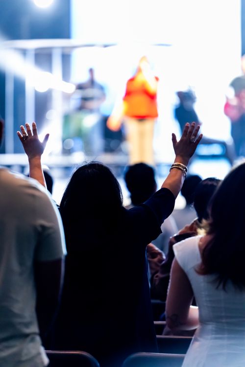 Free Concertgoers raise hands enjoying a live music performance with colorful lighting effects. Stock Photo