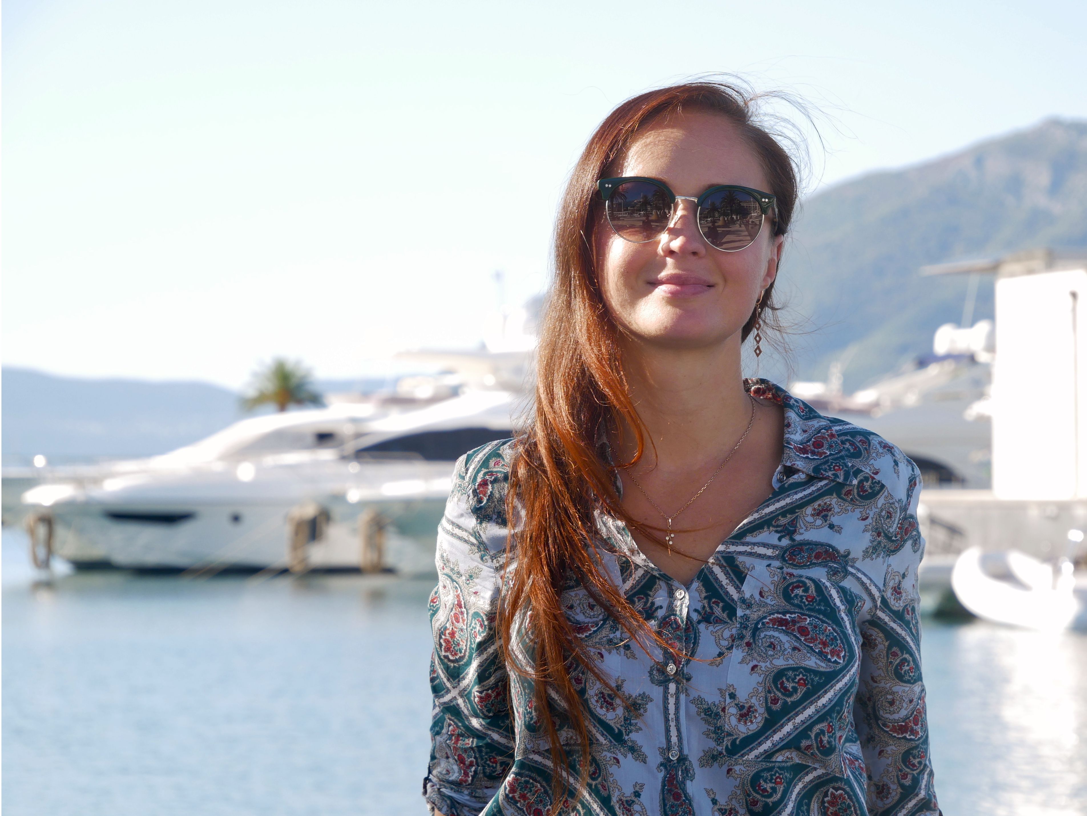 Portrait of a woman in sunglasses at Tivat marina with yachts in the background.
