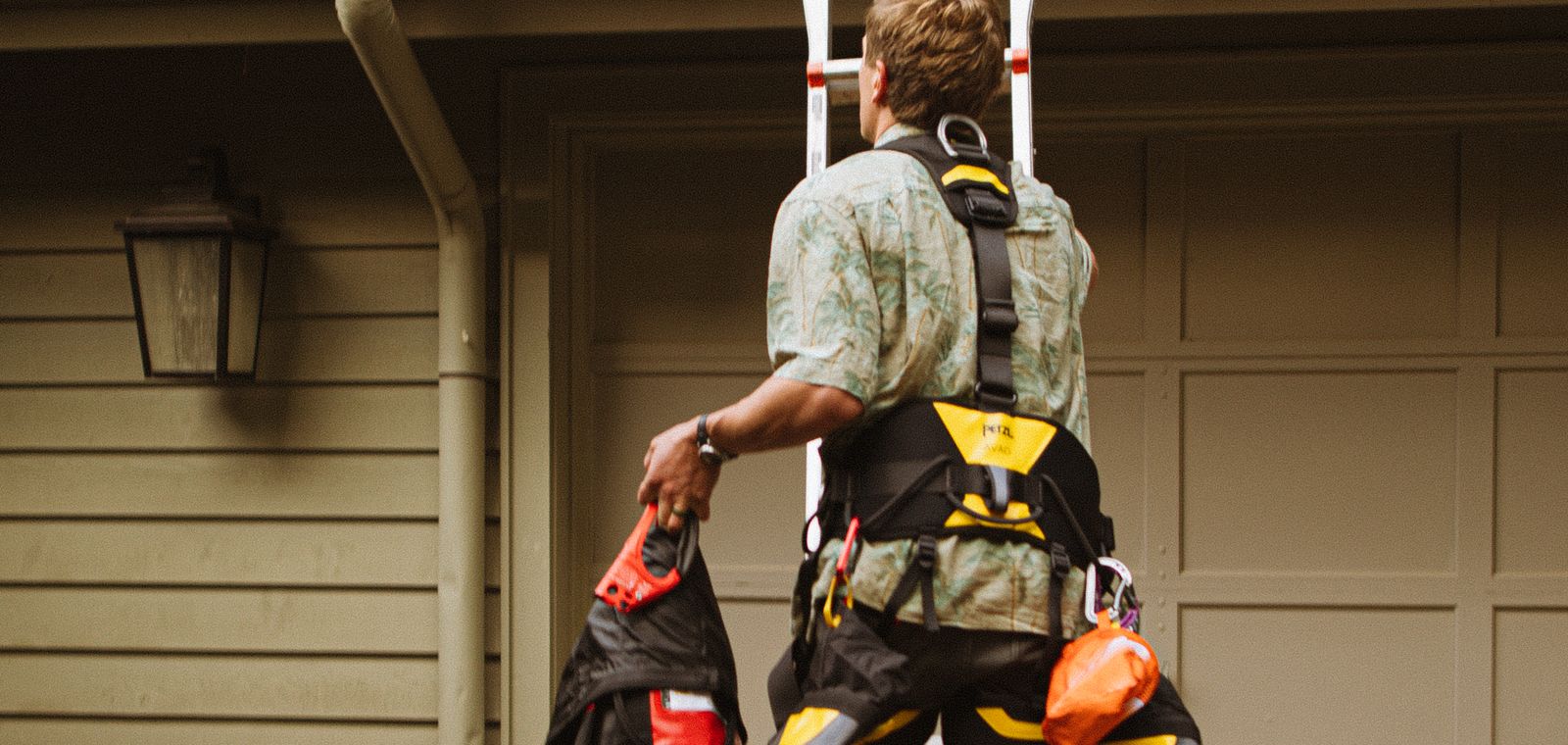 Roofer in a safety harness climbing a ladder to the roof