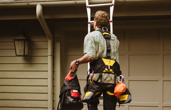 Roofer in a safety harness climbing a ladder to the roof
