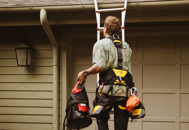 Roofer in a safety harness climbing a ladder to the roof