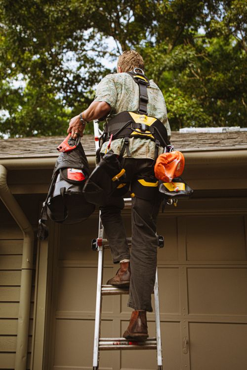 Free A construction worker in safety gear climbs a ladder to perform roof repairs on a home. Stock Photo