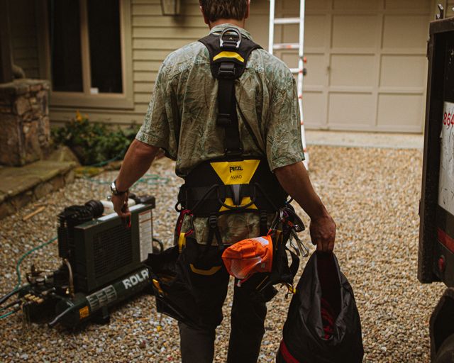 Roofer arriving at a home Roofer in safety gear walking up to a house with a ladder
