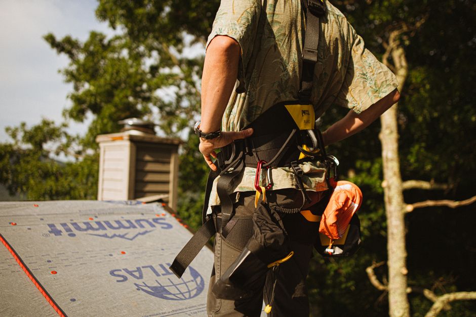 Professional roofer with OSHA safety harness installing roof shingles Professional roofer with OSHA safety harness installing roof shingles