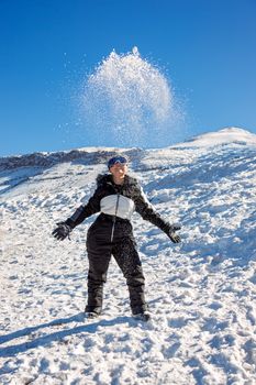Person enjoying a snowy mountain day by tossing snow under a clear blue sky.