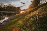 夕阳映照下，河边的景色宁静祥和，远处的草坡和树木被阳光点亮