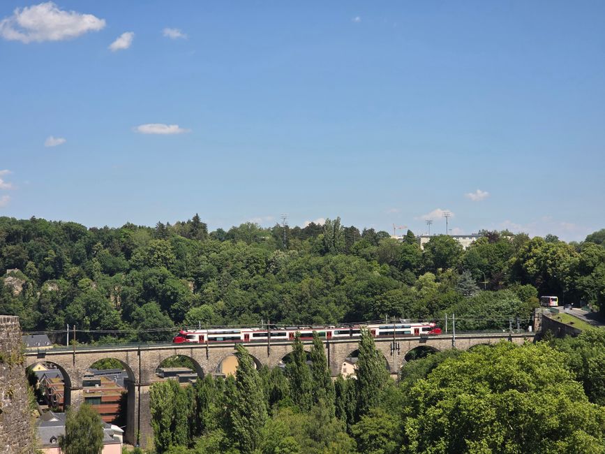 A train crosses the scenic Luxembourg Viaduct on a sunny day.