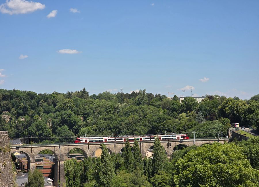 A train crosses the scenic Luxembourg Viaduct on a sunny day.