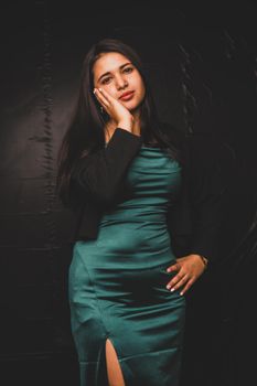 Portrait of an elegant woman in a teal dress, posing against a dark backdrop.