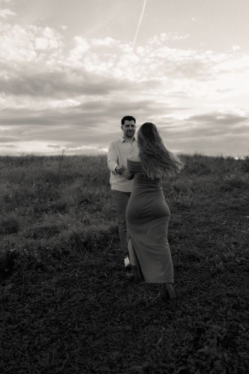 Free A couple joyfully dances in an open field under a dramatic cloudy sky, capturing a moment of connection and romance. Stock Photo