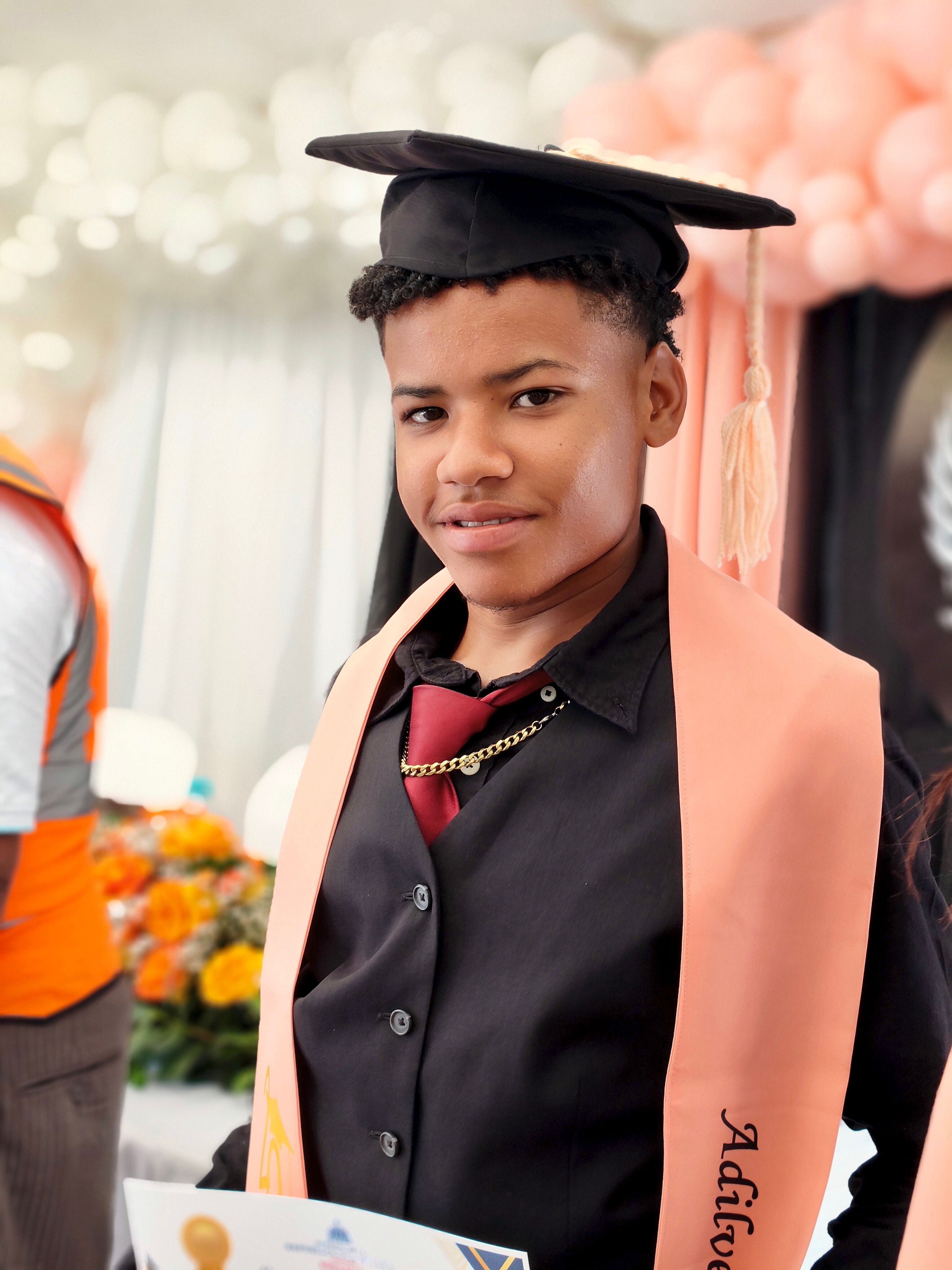 A young adult graduate smiles proudly at a ceremony indoors.