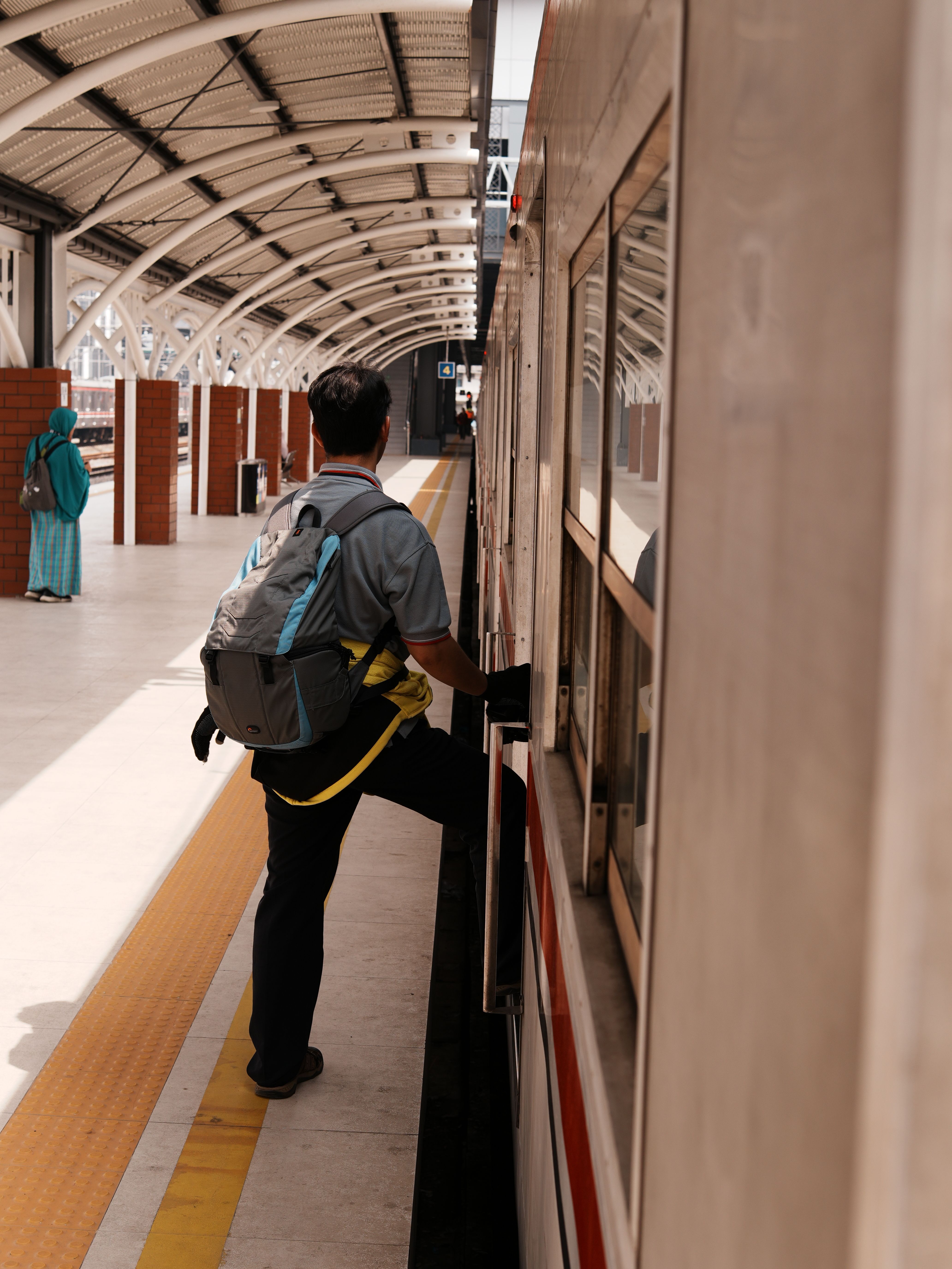 A commuter wearing a backpack boarding a train at an urban station