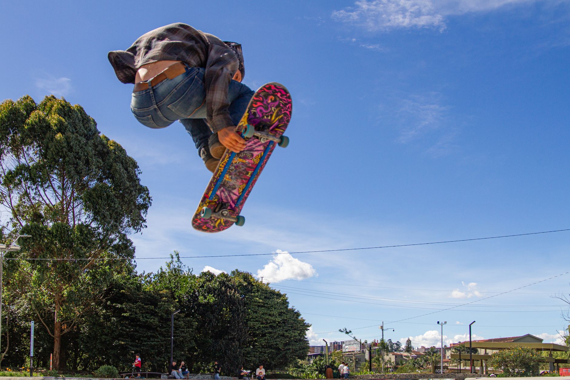 A skateboarder captures a mid-air trick against a clear blue sky in an urban park setting.. skateboarder, captures, trick