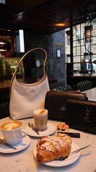 Elegant cafe scene featuring luxury bags, coffee, and a delicious pastry on a marble table.