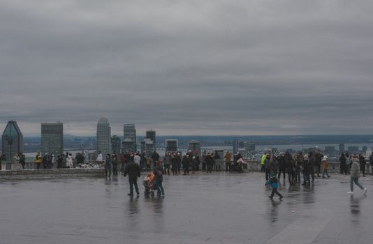 Tourists gather at Mont Royal for a breathtaking view of the Montreal skyline on a cloudy day.