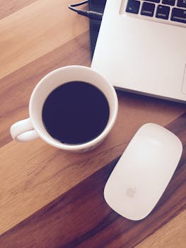 A cup of black coffee next to a laptop and mouse on a wooden desk, perfect for home office vibes.