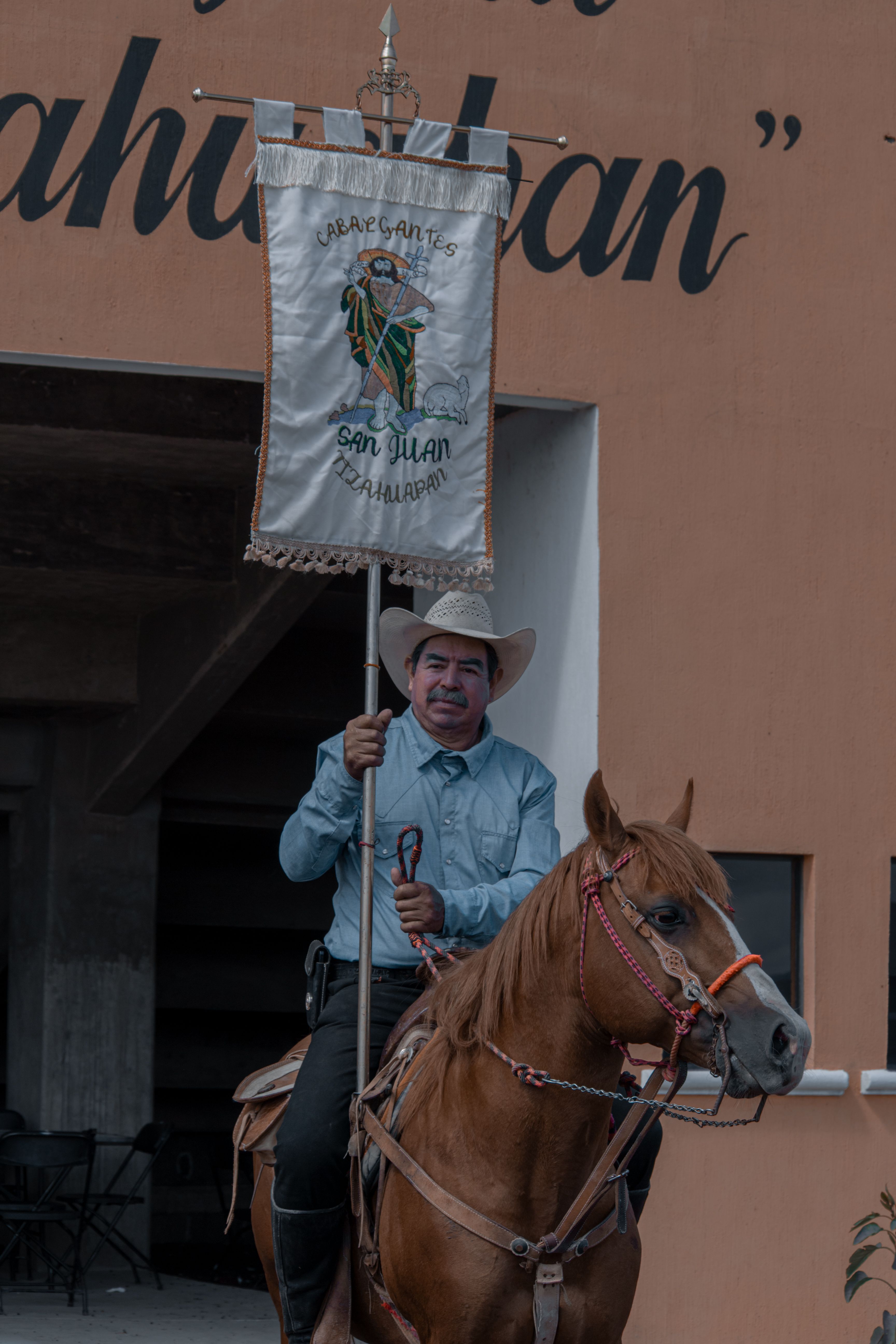 A man on horseback proudly carries a San Juan banner during a cultural event.