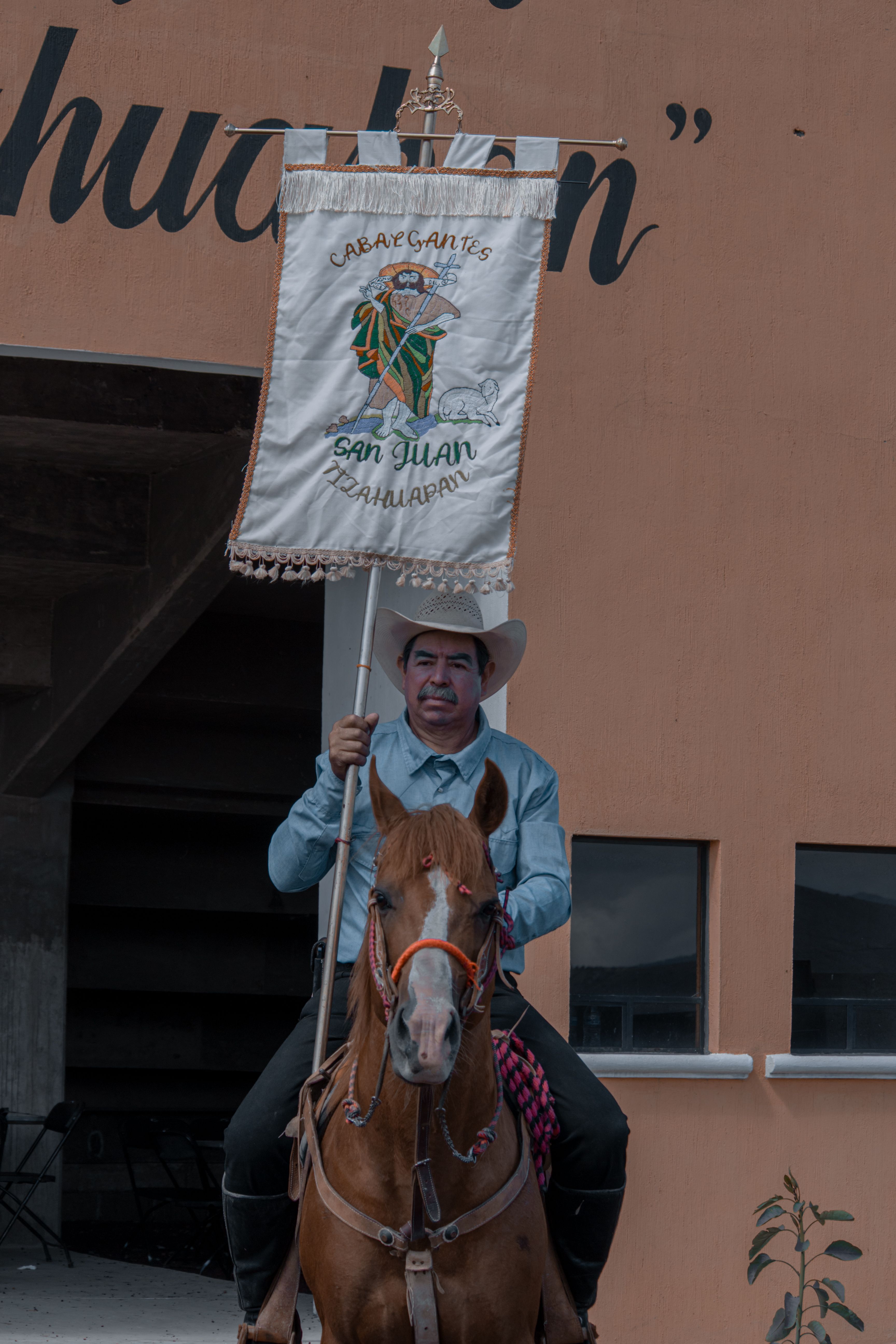 A man in traditional attire on horseback holding a decorated banner in a cultural setting.