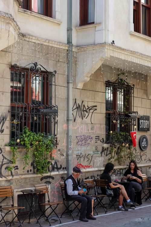 Free Urban cafe in Istanbul's lively street with people enjoying outdoor seating next to graffiti-covered wall. Stock Photo
