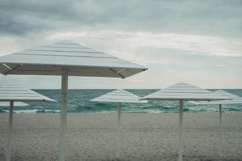 Free Tranquil beach scene with white parasols and a calm ocean, under a cloudy sky. Stock Photo