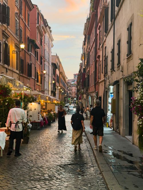 Free Cobblestone street in Rome at dusk with people walking and dining, capturing an authentic Italian atmosphere. Stock Photo