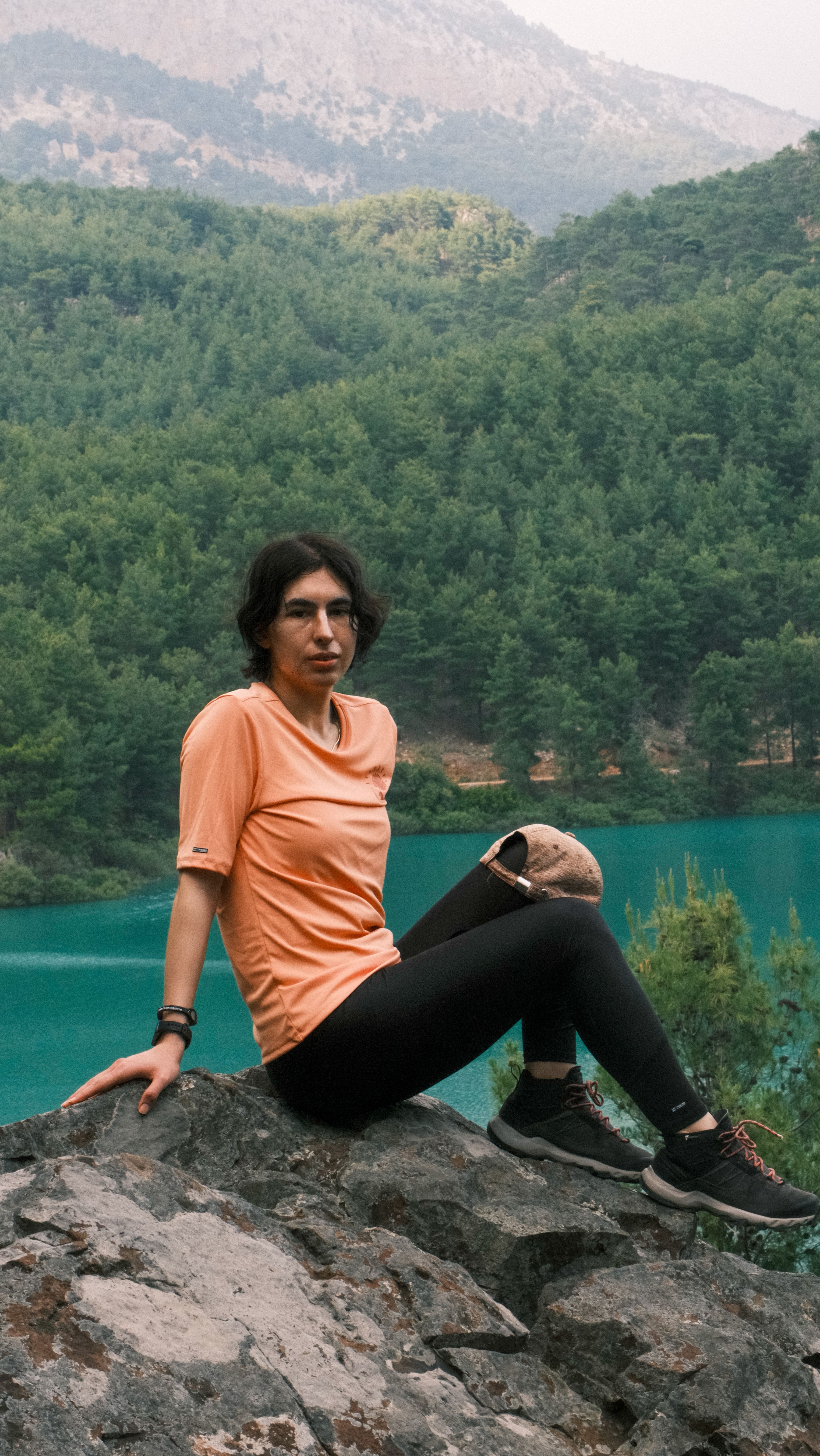 Woman in activewear relaxing on rocks by a serene lake surrounded by forest.
