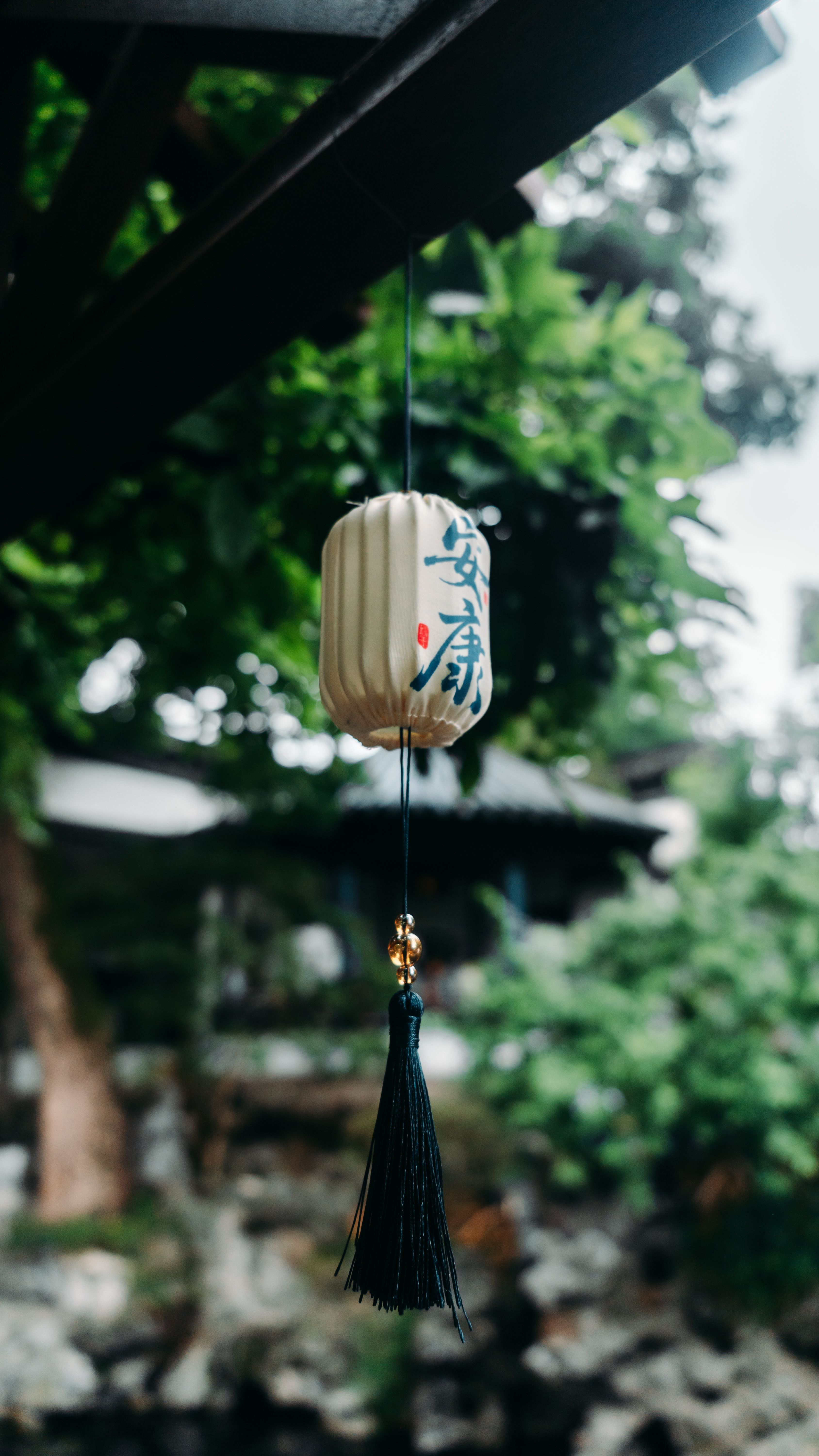 Traditional lantern with Japanese calligraphy hanging outdoors surrounded by greenery.