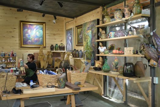 A woman artist meticulously painting a ceramic piece in a vibrant pottery studio full of colorful artwork and vases.