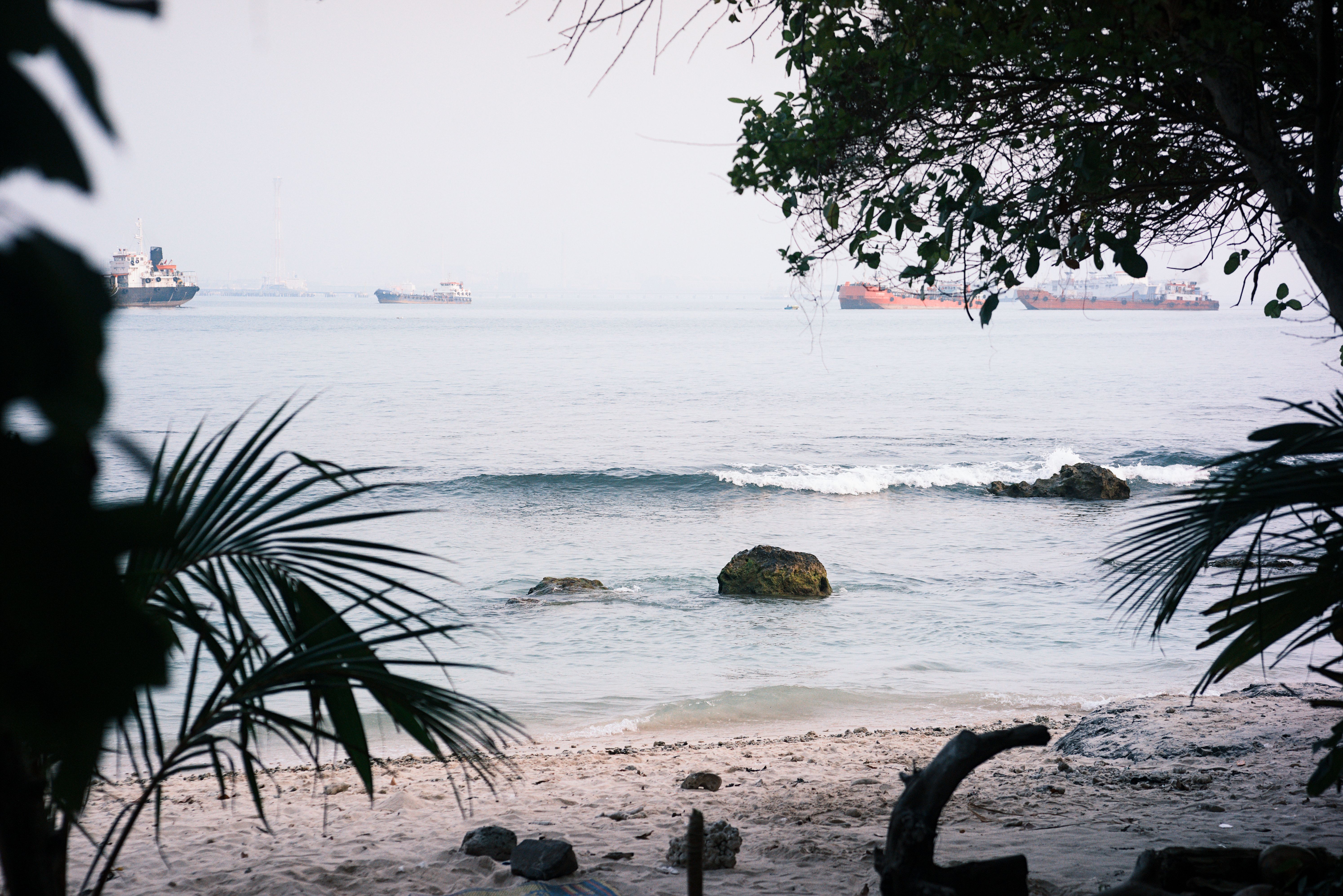 Promenade and narrow sand strip at Fort Kochi Beach with cargo ships on the horizon