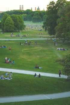 People enjoying a sunny afternoon in a Munich park with greenery and distant city skyline.