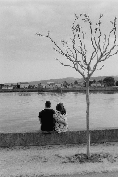 Free A black and white image of a couple sitting by the riverside embracing. Stock Photo